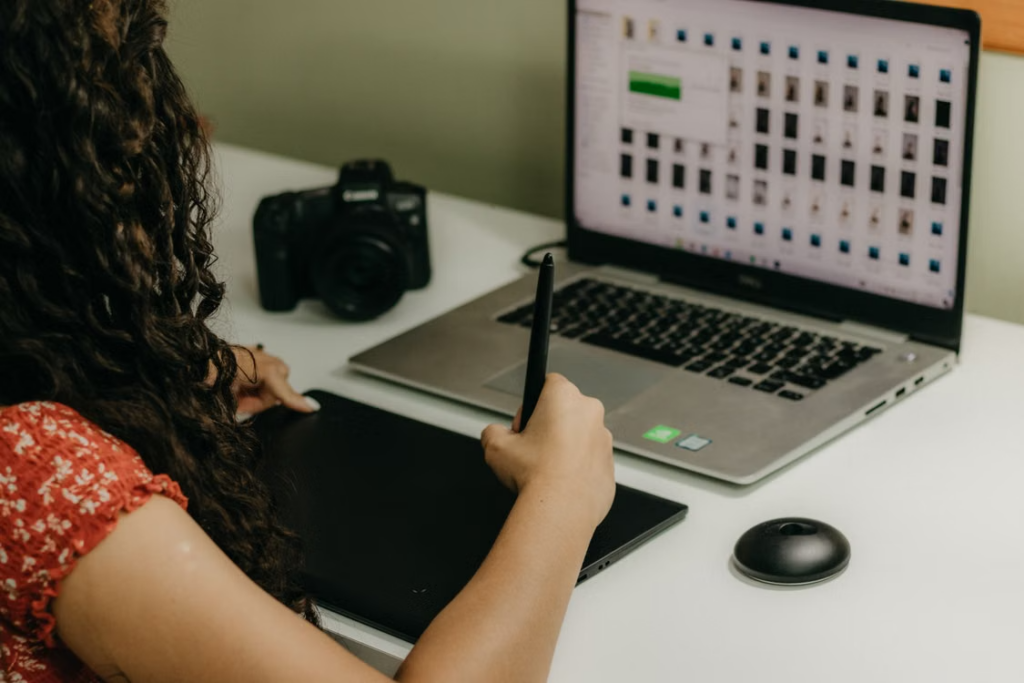 Woman using a pen tablet beside a laptop and camera in a creative workspace